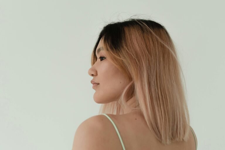 A side view portrait of a woman with light pink balayage hair on a minimalistic background.